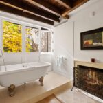 Узкая спальня Millay House с кроватью, балками и окнами на осенние деревья